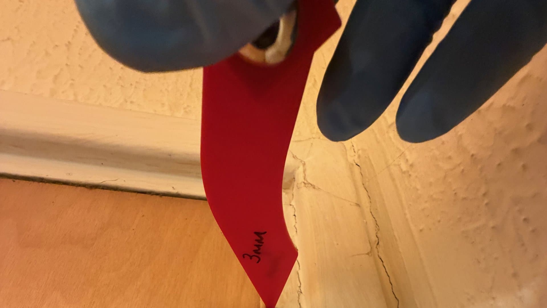 Gloved hand holding a 3 mm gap gauge in the gap at the head of a fire door